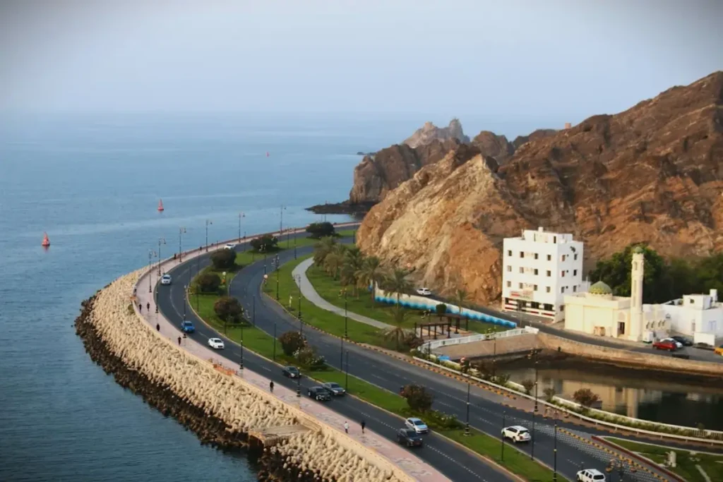 Scenic coastal road in Muscat, Oman, showcasing rugged cliffs, a traditional white mosque, and the Arabian Sea — a perfect glimpse of Oman travel.