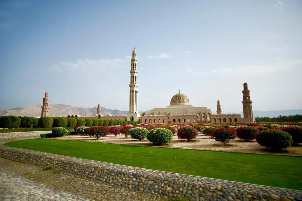 Grand Mosque in Muscat, Oman, with manicured gardens and mountain backdrop under a clear sky – a must-see landmark for Oman travel.








