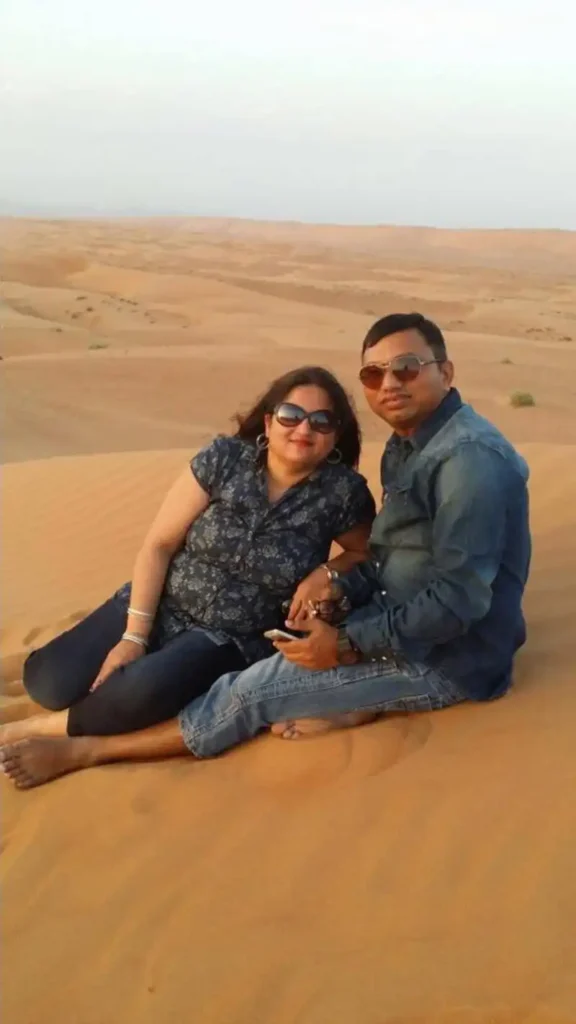 Couple sitting on golden sand dunes in Oman’s desert, enjoying a serene moment during sunset—perfect snapshot of Oman travel experiences.