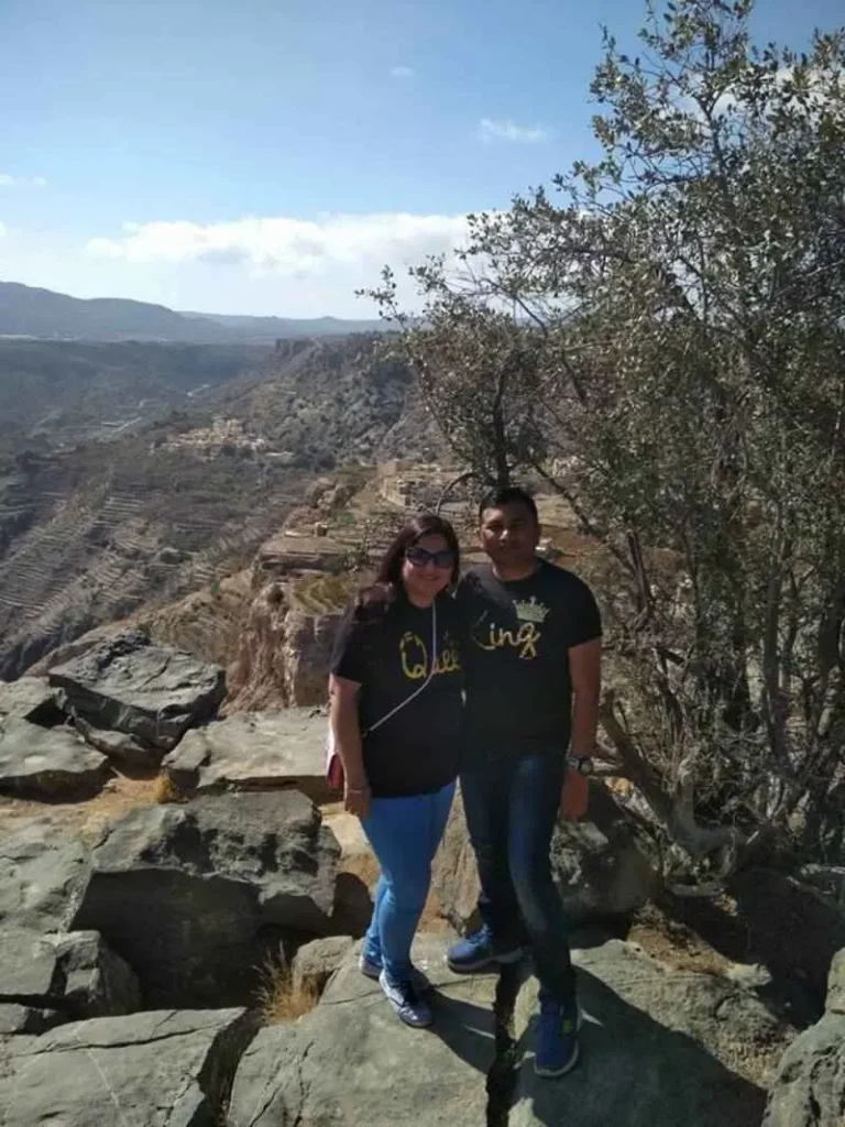 Couple posing at a panoramic viewpoint overlooking terraced mountains and villages in Jebel Akhdar, showcasing one of the best things to do in Oman.