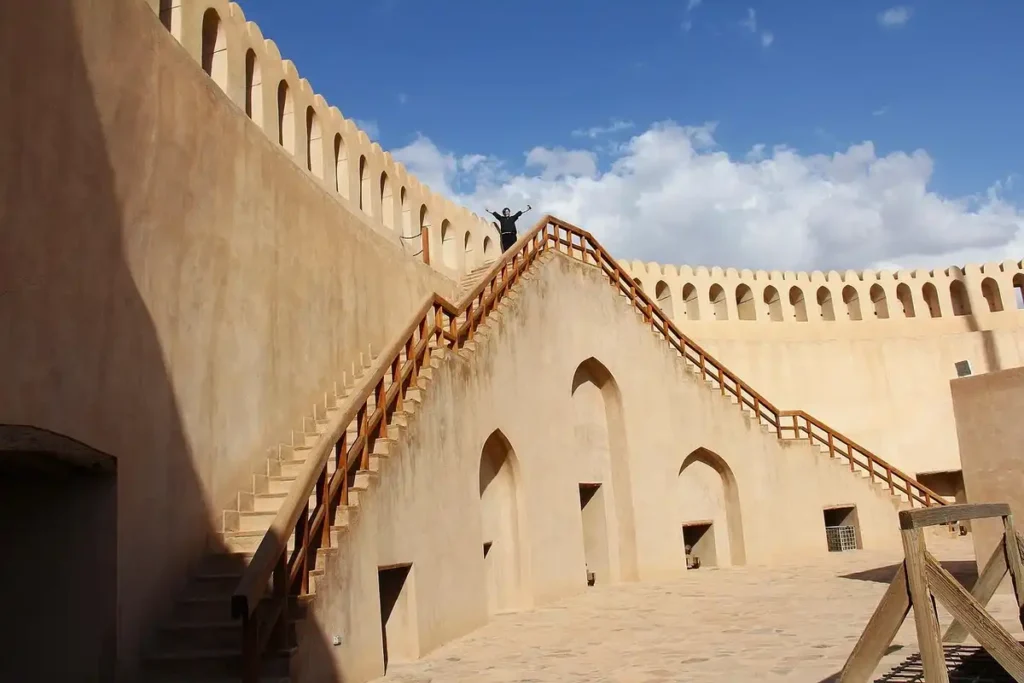 Historic Nizwa Fort in Oman with a person standing triumphantly on the ramparts under a bright blue sky — one of the best things to do in Oman.
