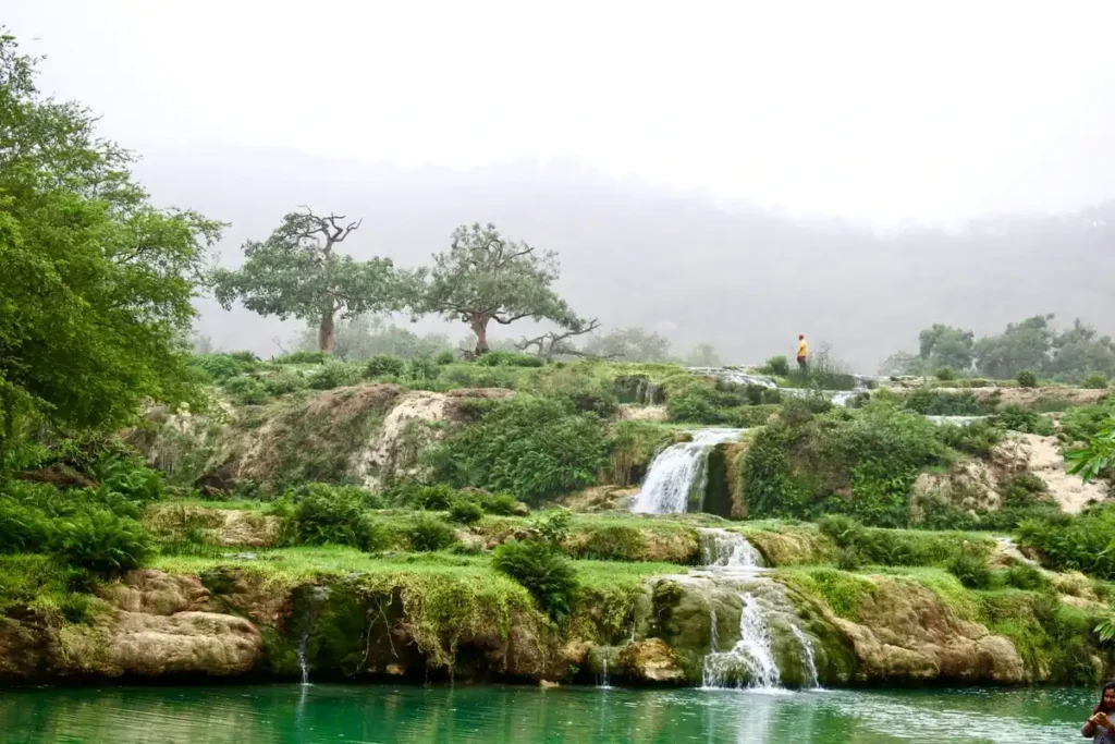 Lush green tiered waterfalls surrounded by tropical vegetation in Salalah, one of the best things to do in Oman during the monsoon season.