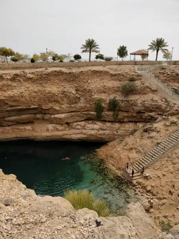 Visitors swimming in the turquoise waters of Bimmah Sinkhole surrounded by rugged limestone cliffs and palm trees – a natural wonder on an Oman travel adventure