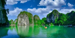 Scenic view of Ha Long Bay with limestone karsts, green waters, and kayakers under a bright blue sky in Vietnam.- Backpacking Vietnam