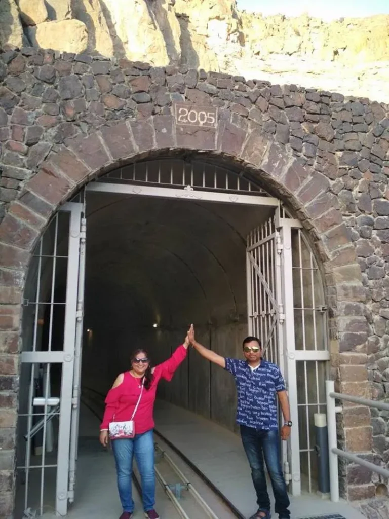A smiling couple giving a high five in front of a historic stone tunnel entrance with “2005” engraved, during their Oman travel adventure.